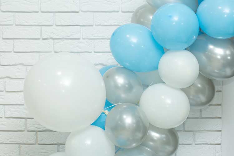 White, silver, and blue balloon arch against white brick wall