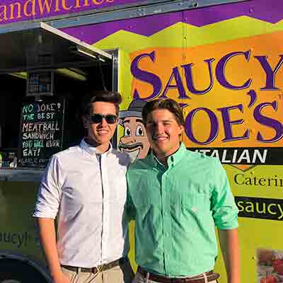 Two guys at a graduation party with Saucy Joe's Food Truck