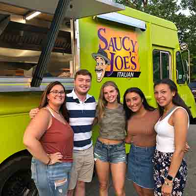 Smiling teens in front of Saucy Joe's Food Truck at graduation party