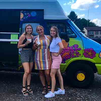 Three graduates in front of gelato truck with cups of ice cream