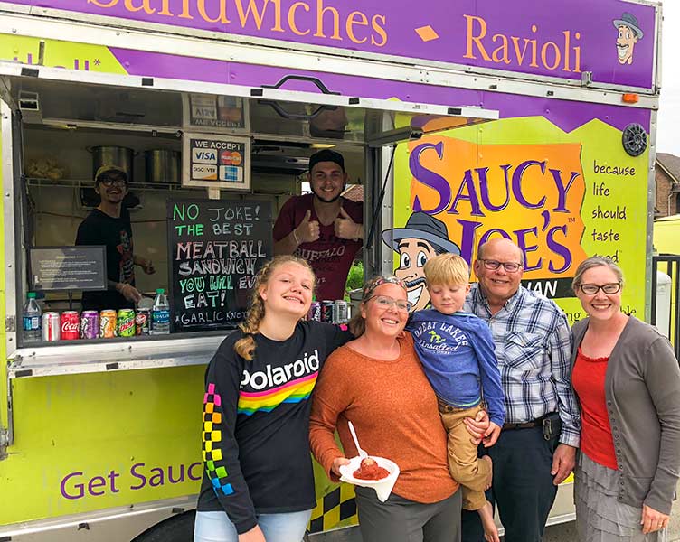 Happy family smiling with Saucy Joe's employees at home retirement party