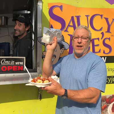 Man smiling in front of Saucy Joe's Food Truck with food