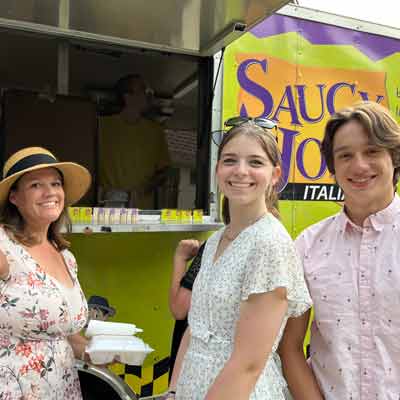 Woman and teens smiling in front of Saucy Joe's Food Truck at party