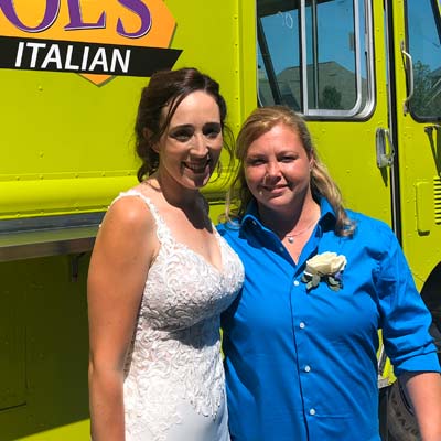 Smiling brides in front of Saucy Joe's Food Truck at wedding